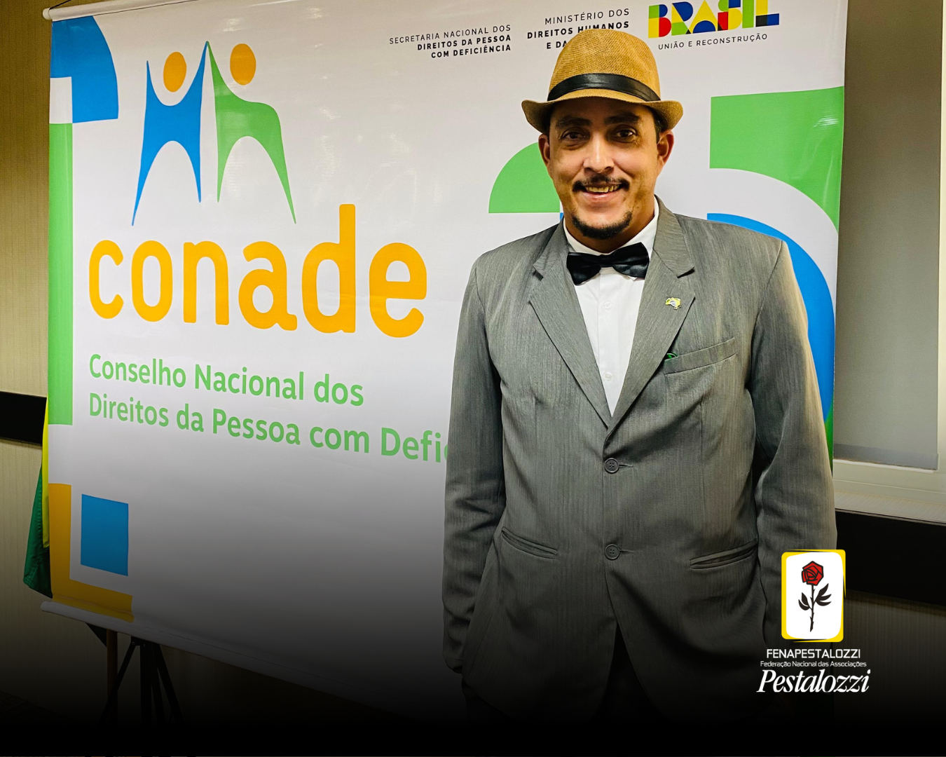 Foto com a parte inferior suavemente escurecida, com a marca institucional no canto inferior direito. Na foto, Jonas Pontes, um homem pardo, está de pé diante de um banner com a marca do Conade. Jonas é um homem pardo, que veste um terno cinza e gravata borboleta e está com um chapéu de cor caramelo.