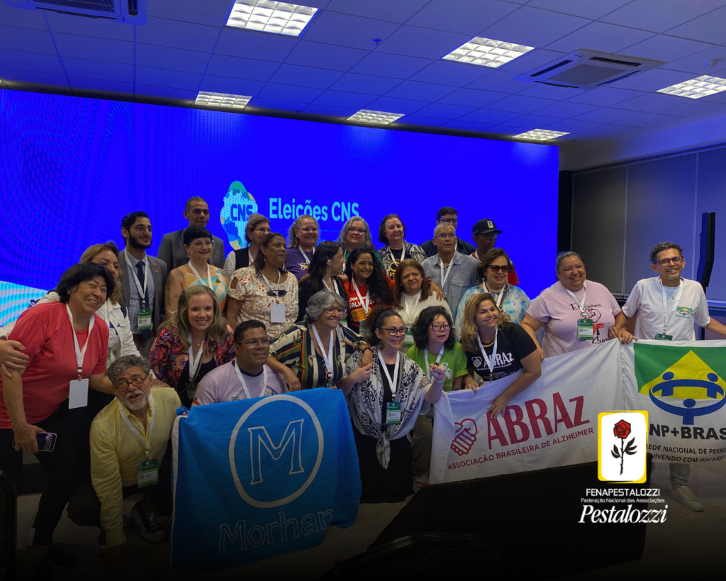 Fotomontagem com degradê escuro na parte inferior. No canto inferior direito há a assinatura com a marca completa da Federação Nacional das Associações Pestalozzi com o ícone do Movimento Pestalozziano: um botão de roseira na cor vermelha, caule, folhas e contornos na cor preta. Este botão está envolvido em uma moldura amarela com fundo branco. Ao centro, foto em grupo com candidatos ao CNS. Eles estão em grupo, formando três filas. Atrás deles um painel de led azul com o texto: Eleições CNS 2024-2027 e a marca do Conselho. na primeira fila de pessoas, há algumas bandeiras de movimentos sociais.