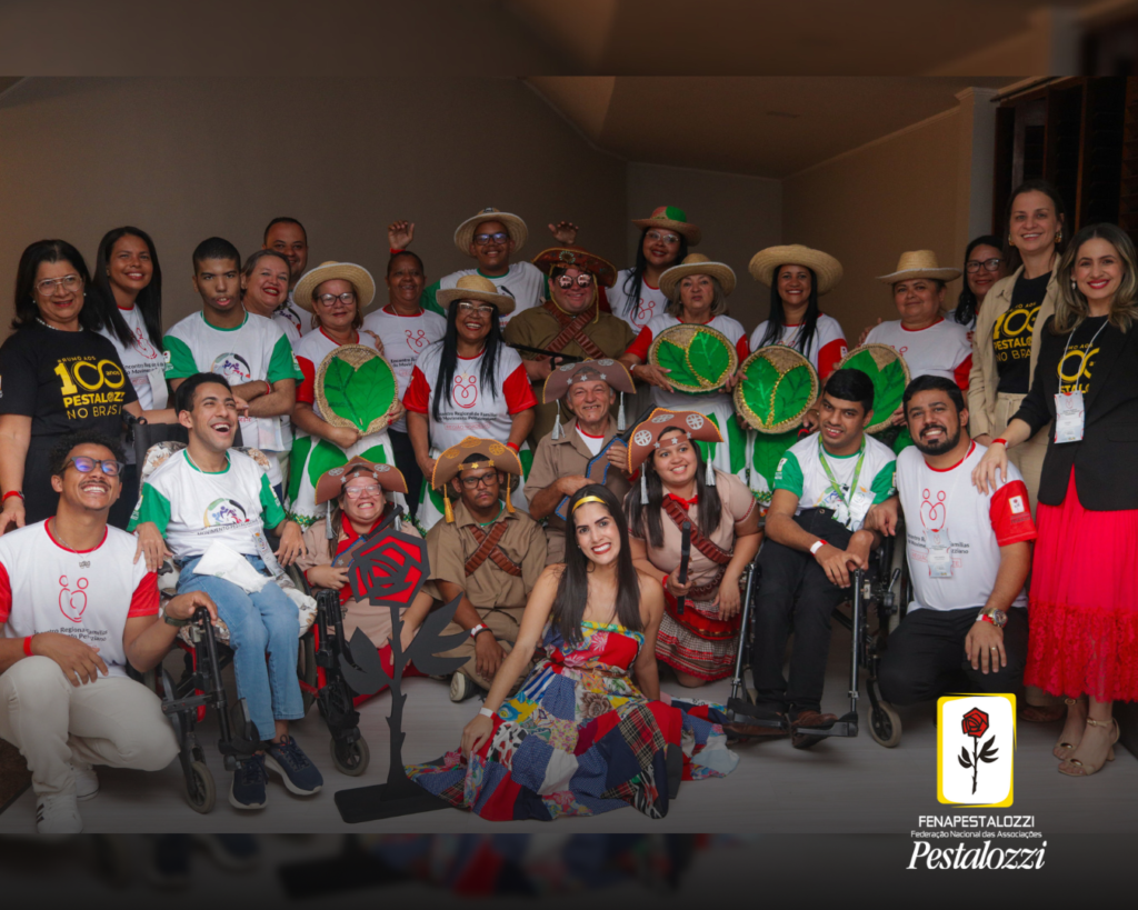 Fotomontagem. No canto inferior direito há a marca completa da Federação Nacional das Associações Pestalozzi com o ícone do Movimento Pestalozziano: um botão de roseira na cor vermelha, caule, folhas e contornos na cor preta. Este está envolvido em uma moldura amarela com fundo branco. Ao centro, foto em plano geral de autodefensores vestidos com a camiseta do evento, branca com mangas verdes; e outros com figurino da peça teatral, coloridos e com chapéu sertanejo.