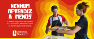 A imagem é um banner horizontal de publicidade ou campanha. Do lado esquerdo, sobre um fundo vermelho, há um texto em letras grandes e brancas que diz "NENHUM APRENDIZ A MENOS". Abaixo, em letras menores, a frase "A defesa inegociável dos direitos e a luta contra o retrocesso social na aprendizagem profissional.". No canto inferior esquerdo, há um logotipo com uma rosa vermelha e o nome "FENAPESTALOZZI Federação Nacional das Associações Pestalozzi" e "Pestalozzi". O lado direito do banner é dominado por uma fotografia de duas pessoas em um ambiente de trabalho. A pessoa à esquerda é um homem usando um boné escuro, uma camisa branca com mangas vermelhas e um avental preto. Ele tem uma expressão concentrada e está olhando para baixo. A pessoa à direita é uma mulher com óculos e cabelo preso, vestindo uma camiseta preta e um avental. Ela está segurando uma tela ou moldura de madeira, aparentemente em um processo de fabricação de papel. O homem está com a mão estendida, como se estivesse ajudando ou orientando. O fundo por trás das duas pessoas é um padrão abstrato de arcos e camadas em tons de laranja e amarelo, criando um efeito de profundidade.