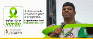 Banner do Setembro Verde. À esquerda, em um fundo branco, há um logo com uma fita verde, um símbolo de conscientização. Abaixo da fita, lê-se "setembro verde". Mais abaixo, um logo da FENAPESTALOZZI, com uma rosa vermelha e o texto "Federação Nacional das Associações Pestalozzi". No centro, sobre o fundo branco, o texto "A diversidade é a chave para o progresso. Capacitismo, não! Capacidades, sim!". À direita, um homem sorridente com deficiência, vestido com uma camisa branca e verde, fala em um microfone. Ele tem cabelo escuro curto e barba por fazer, e sua pele é morena. O fundo da imagem é verde, com uma faixa verde escura que se curva horizontalmente da direita para o centro. Na parte inferior, uma faixa amarela se estende por todo o banner.